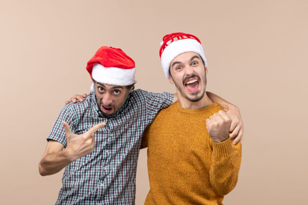 两个前视图两个热情的家伙与圣诞帽拥抱对方米色孤立的背景帽子圣诞老人男人