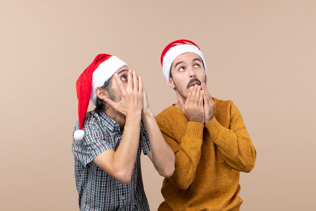 帽子正面图两个戴着圣诞帽的男人在孤立的背景下饶有兴致地看着什么东西惊奇男性二