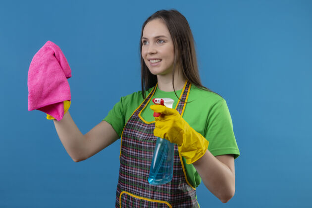 手套微笑的清洁年轻女孩穿着制服 戴着手套 拿着清洁工具和抹布 背景是孤立的蓝色年轻女孩抹布