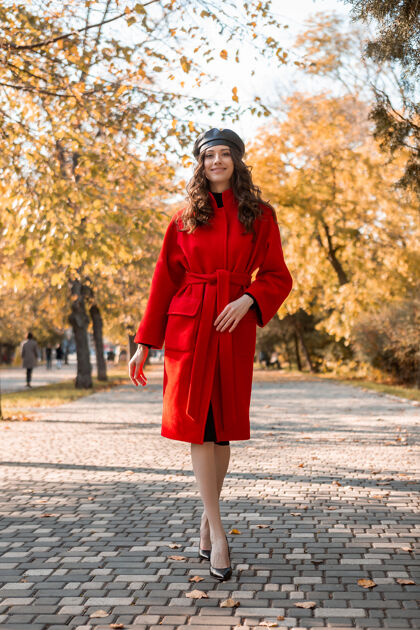 年轻迷人时尚的微笑瘦削女子卷发漫步公园穿着温暖的红色外套秋季时尚 街头风格 戴贝雷帽女性欢快服装