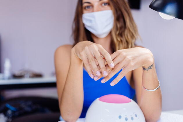 冠状病毒在美容院戴着医用防护口罩的女士拿着调色板 选择一种颜色的美甲程序美甲护理盛大开放检疫结束小企业再次开放护理指甲指甲