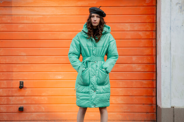 街头风格穿着冬秋时尚潮流蓬松外套和帽子贝雷帽的时髦女人在街上对着橙色的墙壁摆姿势街头服装户外
