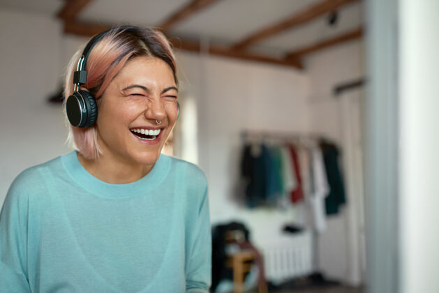 肖像开朗积极的年轻女博主一边用耳机录制播客 一边用鼻环大笑休闲无线科技