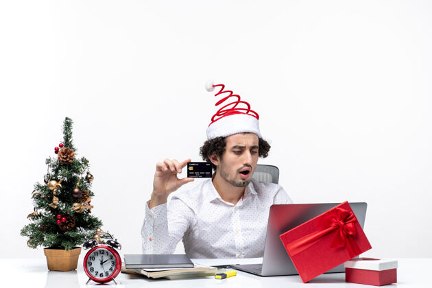 圣诞老人节日喜庆的气氛 惊讶的商人戴着圣诞老人的帽子 拿着银行卡独自在白色背景的办公室里做项目帽子商务人士单独