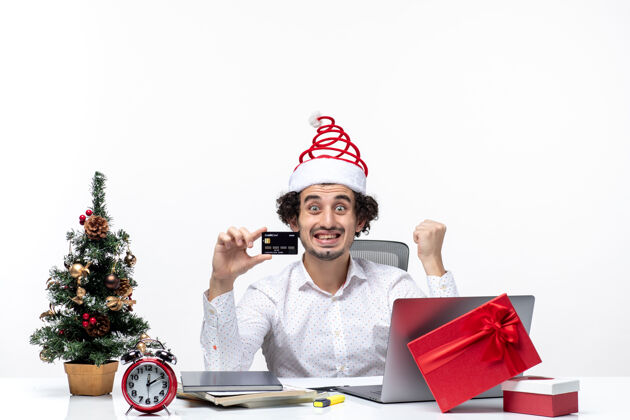 节日节日喜庆的气氛 惊讶的商人戴着圣诞老人的帽子 拿着他的银行卡在白色背景的办公室里人圣诞节商务