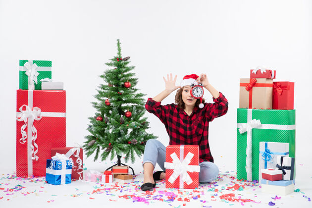 坐着前视图的年轻女子坐在圣诞礼物周围拿着白色墙上的时钟节日人礼物