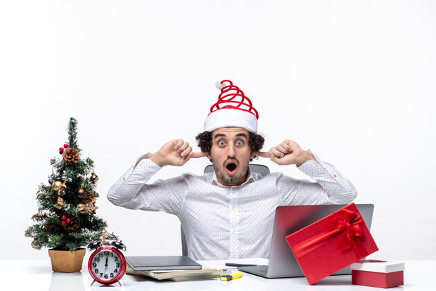 耳朵震惊的年轻商人戴着滑稽的圣诞老人帽子庆祝圣诞节 在白色背景的办公室里闭上耳朵 阻止别人聆听圣诞老人商人防止