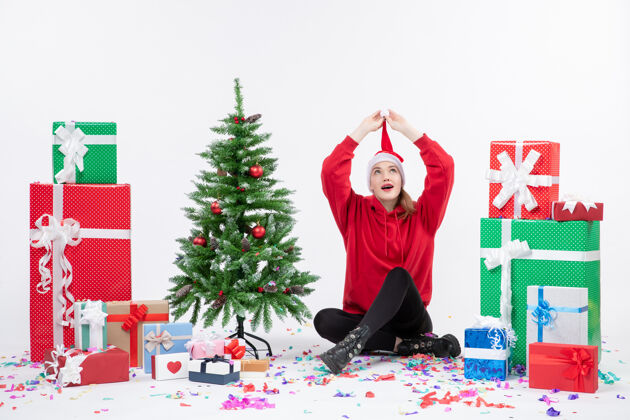 圣诞快乐年轻女子围坐在白色墙壁上的礼物前视图帽子前面庆祝