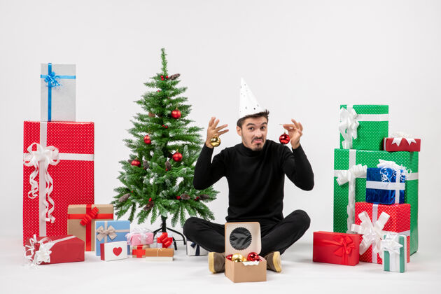 抱着正面图：年轻人围坐在白色的墙上 手里拿着圣诞礼物礼物圣诞树玩具