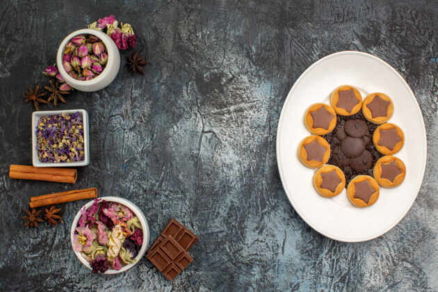景观白色盘子上的饼干和灰色地面上的干花和巧克力碗的俯视图食物顶部巧克力