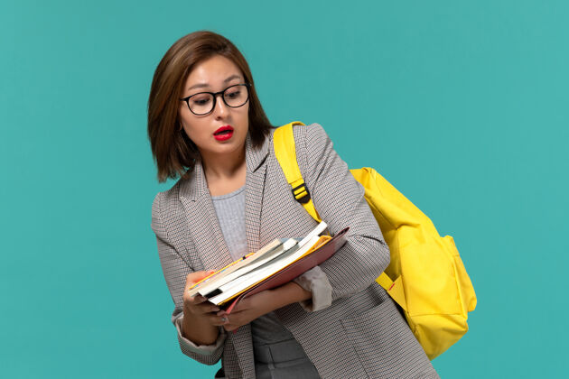 设备身着灰色夹克 黄色背包 蓝色墙壁上拿着书的女学生正面图商务背包Female