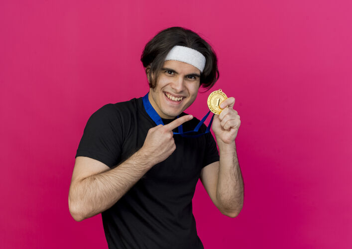 微笑高兴的年轻人穿着运动服 头戴金领 用食指指着奖牌开心地笑着周围穿着男士