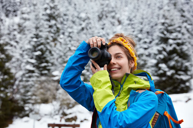 头带快乐的女人在雪山上拍照 在大自然中度过寒假 穿着鲜艳的夹克高山通讯漫步