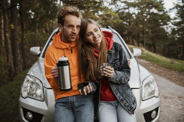 冒险一对夫妇坐在车外的引擎盖上享受热饮料的前视图冒险远足冒险