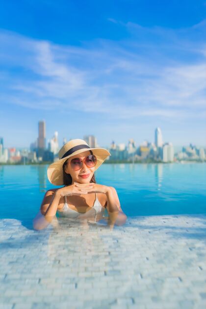 豪华肖像美丽的亚洲年轻女子微笑放松休闲围绕室外游泳池与城市景观度假村城市女性