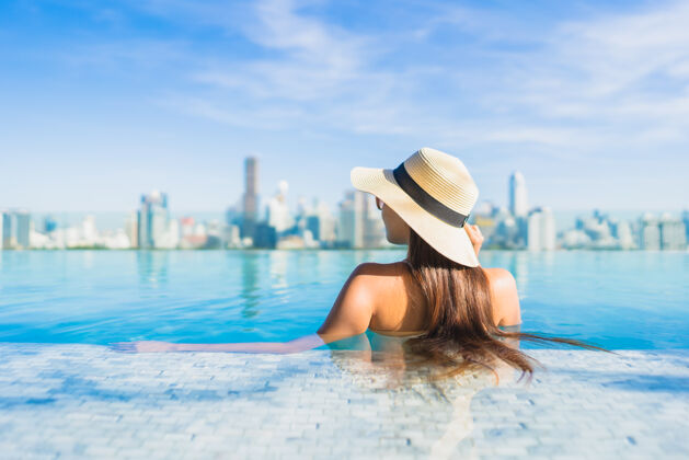 现代美丽的亚洲年轻女子在户外游泳池周围放松 城市景色尽收眼底中心塔楼城市景观