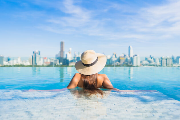 游泳池美丽的亚洲年轻女子在户外游泳池周围放松 城市景色尽收眼底城市外部摩天大楼