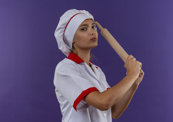 抱着自信的年轻厨师女穿着厨师制服拿着擀面杖站在隔离的墙上 有复制的空间制服女年轻