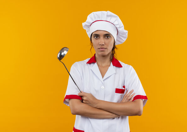 手自信的年轻女厨师穿着厨师制服 双手交叉 拿着勺子 站在隔离的黄色墙壁上 有复制空间勺子自信穿