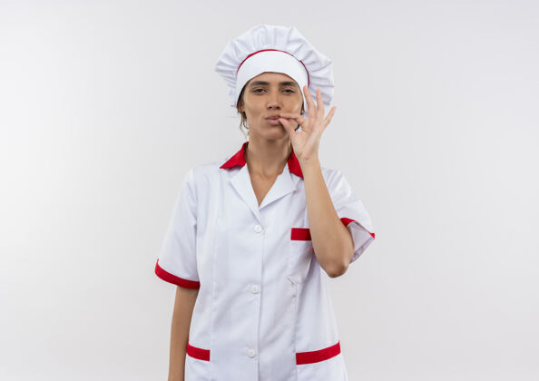 手势穿着厨师制服的年轻女厨师在隔离的白色墙壁上展示着美味的手势 还有复制空间展示女厨师
