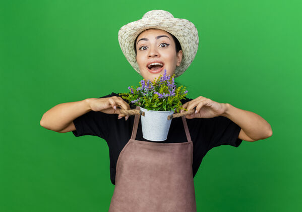 微笑年轻漂亮的女园丁围着围裙 戴着帽子 手里拿着盆栽植物 欢快地笑着帽子园丁看着