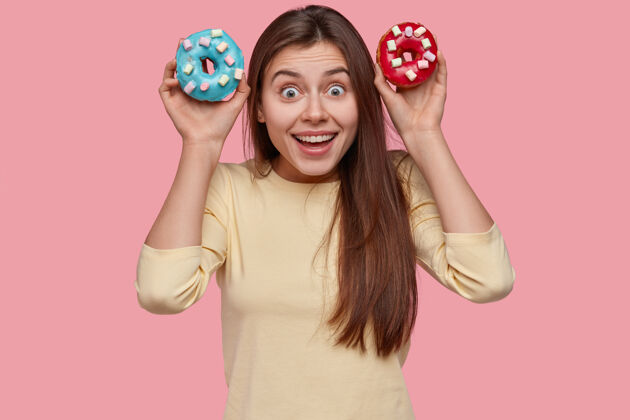 拿着搞笑的黑发女士拿着五颜六色的甜甜圈 直接开心地看着女士快乐食物