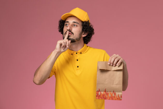 男性快递员正面图穿着黄色制服的男快递员拿着浅粉色墙上的纸质食品包制服粉色男人