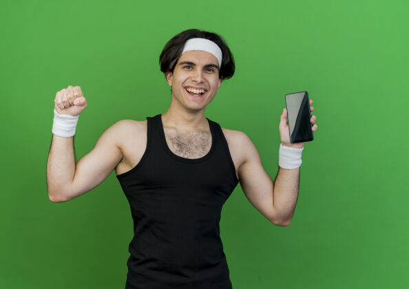 穿着身穿运动服 头戴头巾的年轻运动男展示智能手机握紧拳头的快乐和兴奋运动装年轻头带