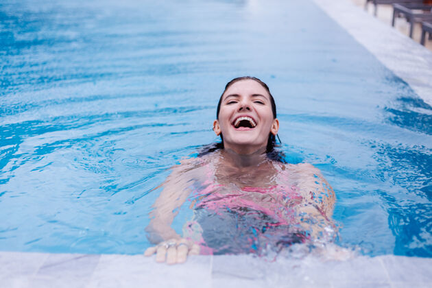 度假在明亮的粉红色比基尼蓝色游泳池里的年轻快乐修长的欧洲女人放松优雅迷人