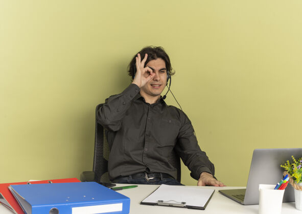 工人年轻自信的上班族戴着耳机坐在办公桌旁 用手指看着笔记本电脑耳机自信办公室
