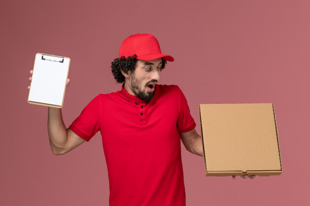 成人正面图：身穿红色衬衫和披风的男性快递员在粉色墙上拿着快递食品盒和记事本人粉色送货