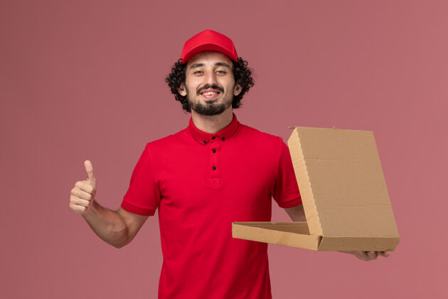 送货正面图穿着红色衬衫和斗篷的男快递员拿着空的送货食品盒 微笑着站在粉红色的墙上男性快递员食物男人