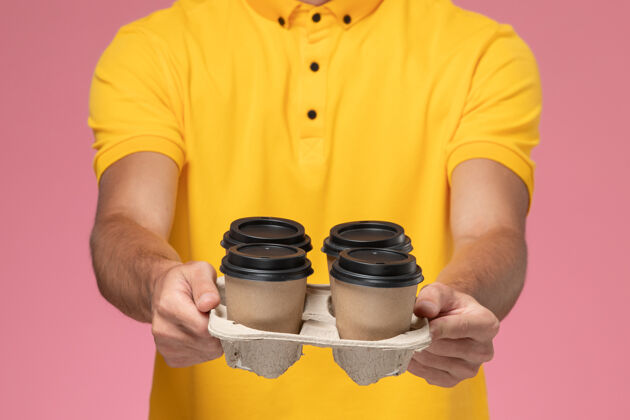 成人正面图穿着黄色制服的男信使拿着棕色的咖啡杯在粉红色的墙上黄色棕色送货