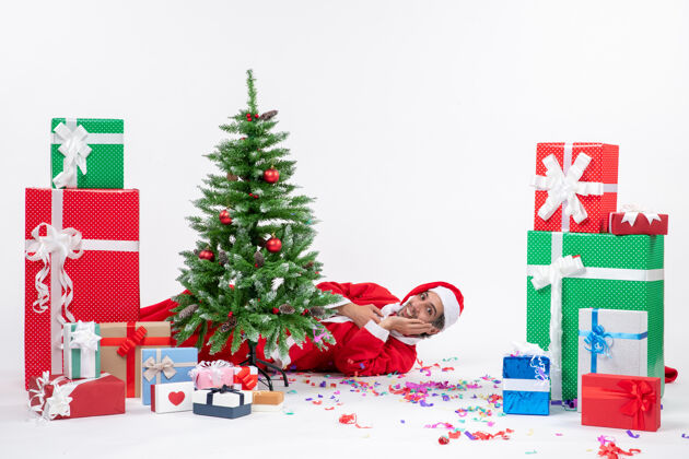 圣诞老人圣诞老人躺在圣诞树后面 在白色背景上有不同颜色的礼物 圣诞气氛喜庆不同冬青礼物