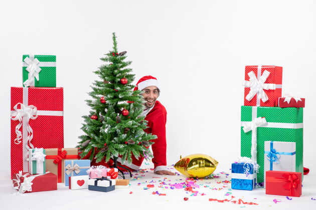礼物圣诞气氛与年轻的圣诞老人躲在圣诞树附近的礼物在白色背景上不同的颜色季节礼物礼物