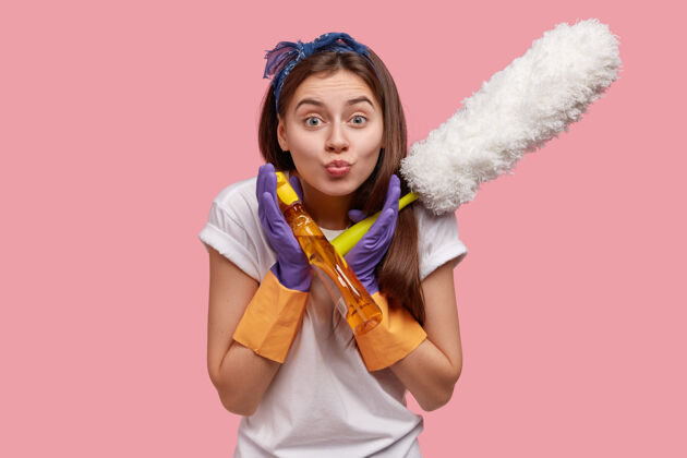 家务忙碌的女人做鬼脸 撅嘴 穿休闲服 拿刷子和清洁剂 做春季清洁凝视喷雾摆姿势