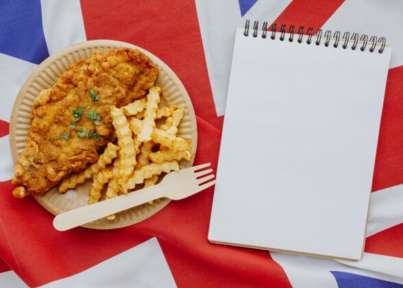 油炸带笔记本和英国国旗的盘子上的鱼和薯条俯视图菜传统英语