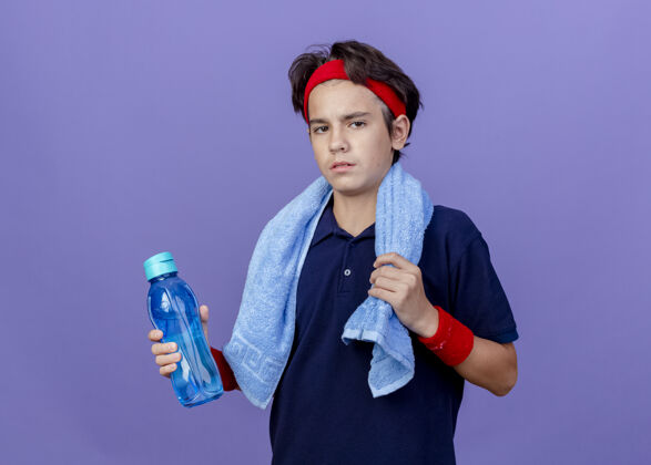 青少年自信的年轻帅气的运动男孩戴着头带和手环 脖子上围着毛巾拿着水瓶抓毛巾看青少年年轻