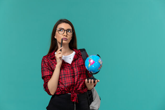 钢笔女学生背着背包 拿着小地球仪和钢笔 站在浅蓝色的墙上大学女学生课