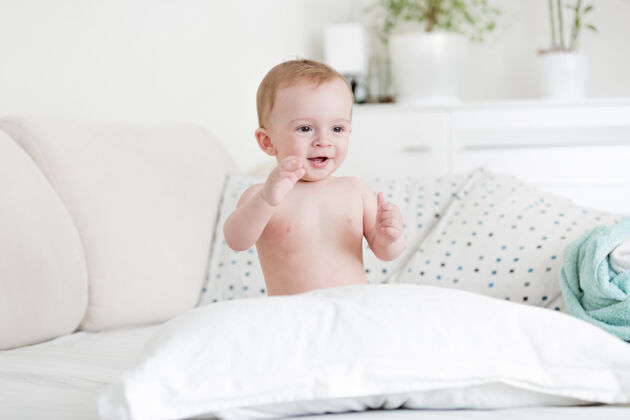 乐趣快乐的裸体男婴在床上玩枕头的画像肖像坐着有趣