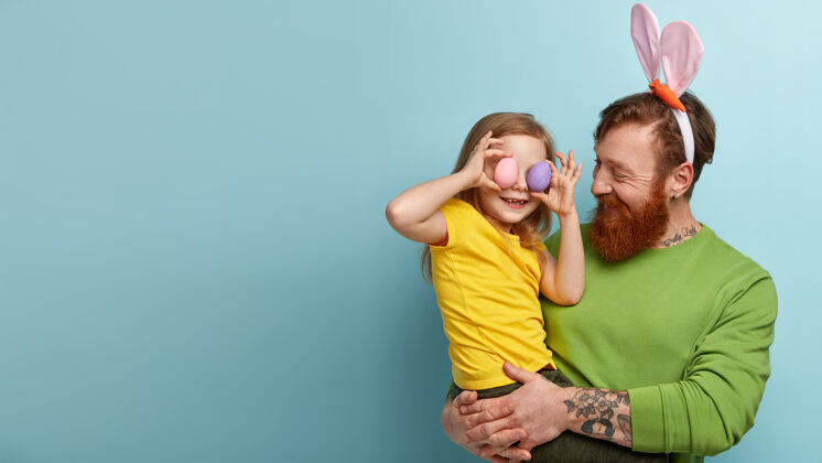 爸爸一个留着姜黄色胡子的男人穿着五颜六色的衣服 抱着女儿的兔子耳朵人人肖像